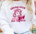 White sweatshirt with pink graphic of a crying woman holding a book and teacup with text 'Crying Over Book Boyfriends'