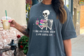 person wearing dark graphic t-shirt with skeleton holding books and iced coffee, text reads 'I like my books spicy & my coffee icy'
